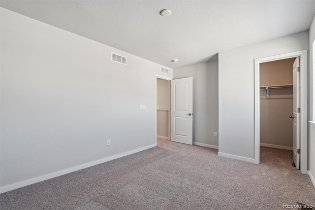 unfurnished bedroom featuring a walk in closet, light colored carpet, and a closet