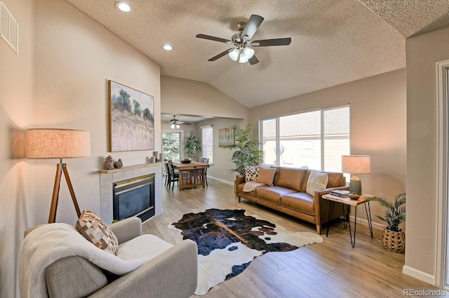 living room with ceiling fan, a textured ceiling, vaulted ceiling, a fireplace, and light wood-type flooring