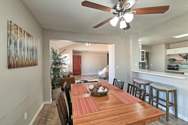 dining space with ceiling fan, sink, and wood-type flooring