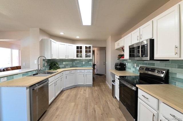 kitchen with light wood-type flooring, tasteful backsplash, stainless steel appliances, sink, and white cabinets