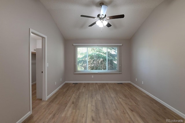 empty room featuring a textured ceiling, light hardwood / wood-style floors, and vaulted ceiling