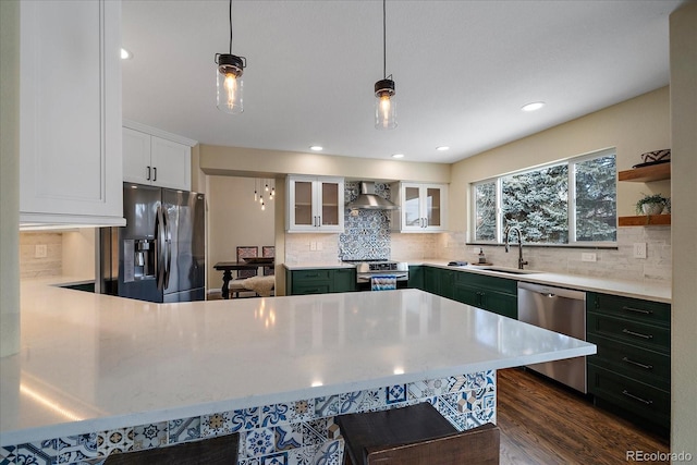 kitchen featuring appliances with stainless steel finishes, white cabinetry, hanging light fixtures, sink, and wall chimney range hood