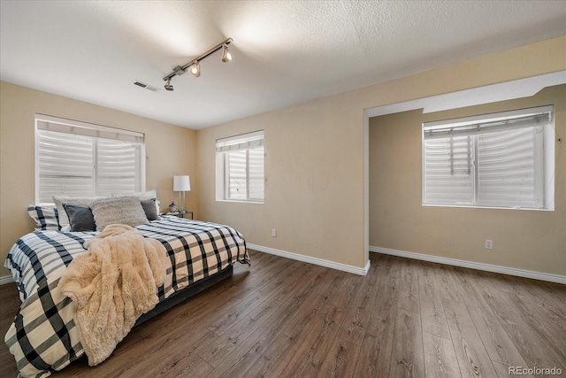 bedroom featuring hardwood / wood-style flooring, rail lighting, and a textured ceiling