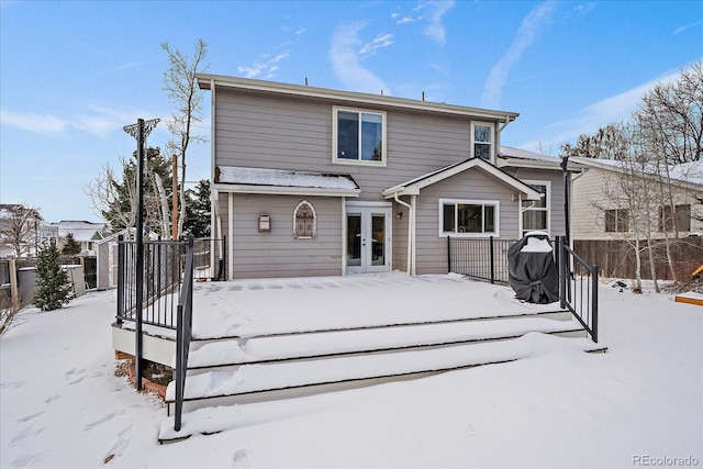 snow covered back of property featuring french doors and a wooden deck