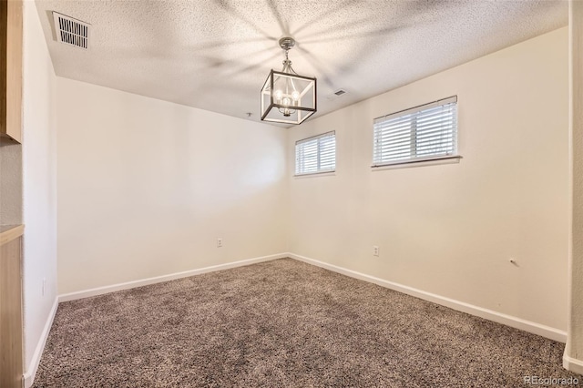 spare room featuring carpet flooring, a textured ceiling, and an inviting chandelier