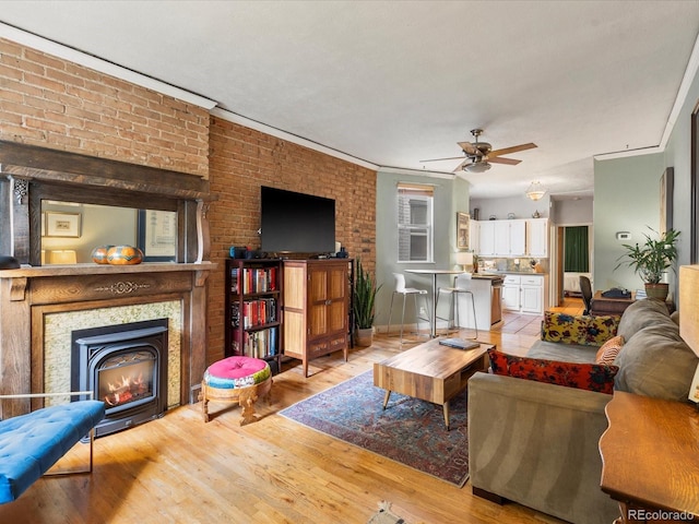 living room featuring ceiling fan, ornamental molding, brick wall, and light wood-type flooring