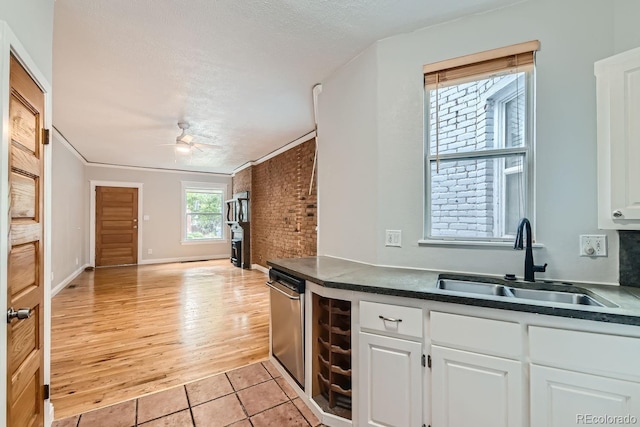 kitchen featuring sink, light tile patterned floors, ceiling fan, white cabinetry, and brick wall