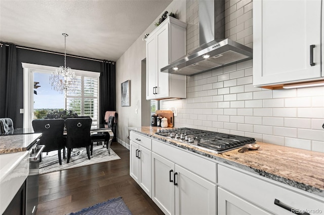10080 E 160th Pl, Brighton, CO 80602 - kitchen with wall chimney exhaust hood, dark wood-style flooring, a chandelier, stainless steel gas cooktop, and white cabinetry