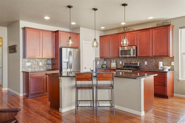 kitchen with hardwood / wood-style flooring, appliances with stainless steel finishes, an island with sink, and pendant lighting