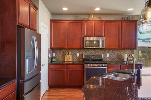 kitchen with sink, light hardwood / wood-style flooring, stainless steel appliances, decorative backsplash, and dark stone counters