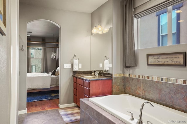 bathroom featuring a relaxing tiled tub, vanity, and tile patterned flooring