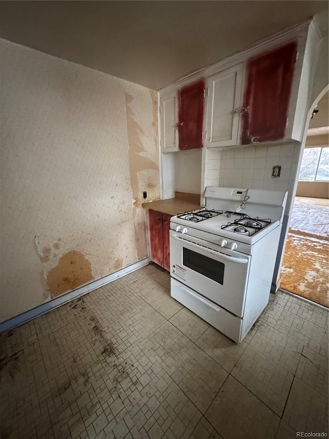 kitchen with white gas range, arched walkways, decorative backsplash, and light countertops