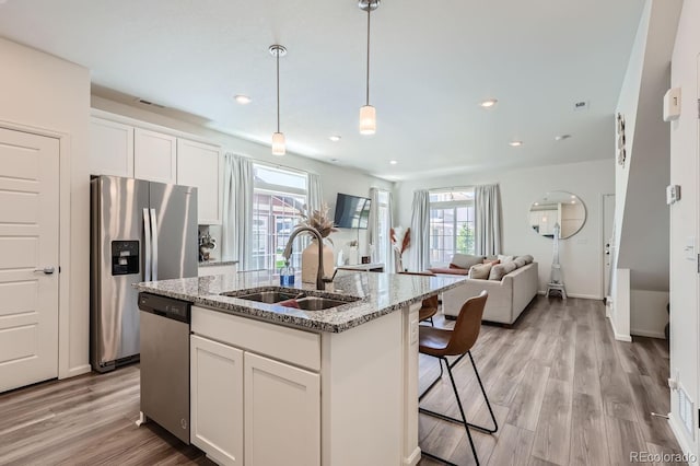 kitchen featuring open floor plan, stainless steel appliances, an island with sink, and white cabinets