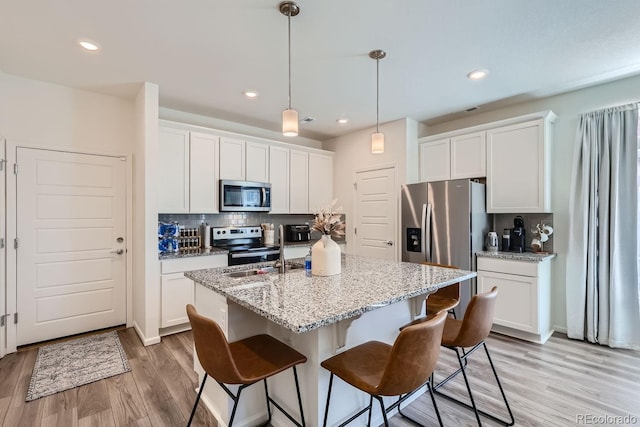 kitchen featuring stainless steel appliances, a kitchen island with sink, white cabinetry, and decorative light fixtures