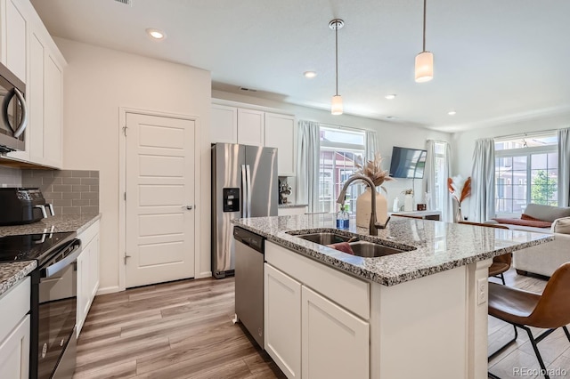 kitchen featuring an island with sink, appliances with stainless steel finishes, decorative light fixtures, white cabinetry, and a sink