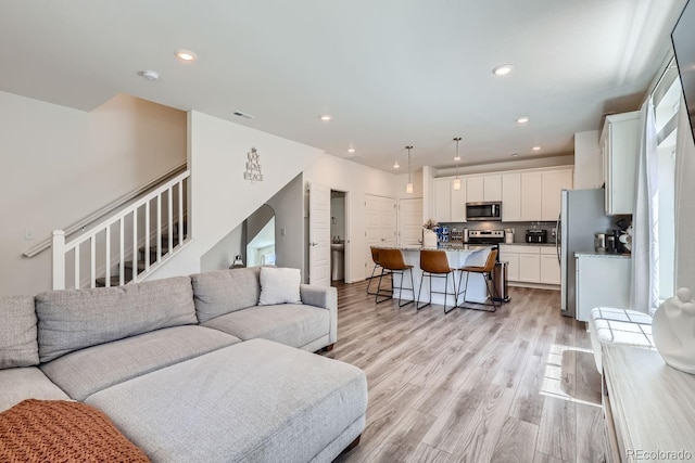 living area featuring arched walkways, recessed lighting, visible vents, light wood-type flooring, and stairs