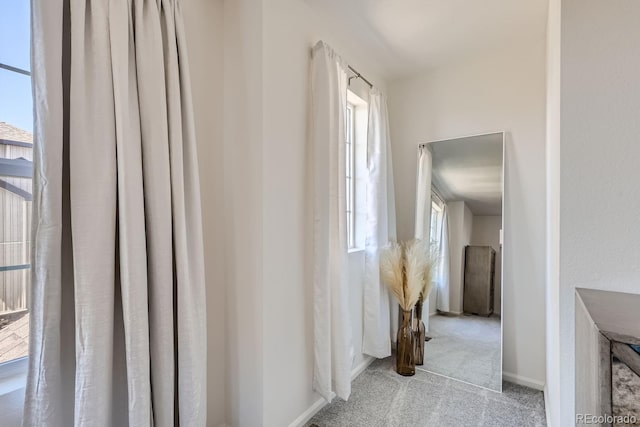 hall featuring baseboards, a healthy amount of sunlight, and light colored carpet