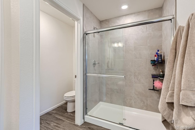 bathroom with baseboards, wood finished floors, toilet, and a shower stall