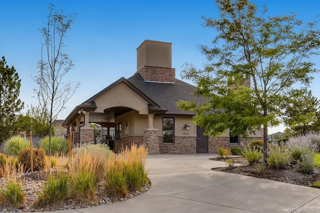 view of front of house featuring driveway, a shingled roof, stone siding, a chimney, and stucco siding