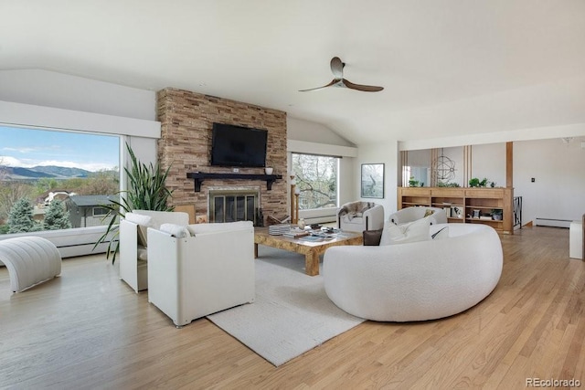 living room with a ceiling fan, vaulted ceiling, a brick fireplace, a mountain view, and light wood-style floors