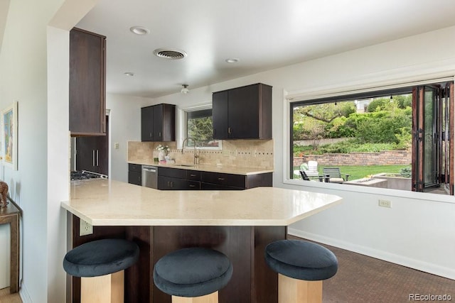 kitchen featuring decorative backsplash, a sink, a peninsula, a breakfast bar, and stainless steel appliances