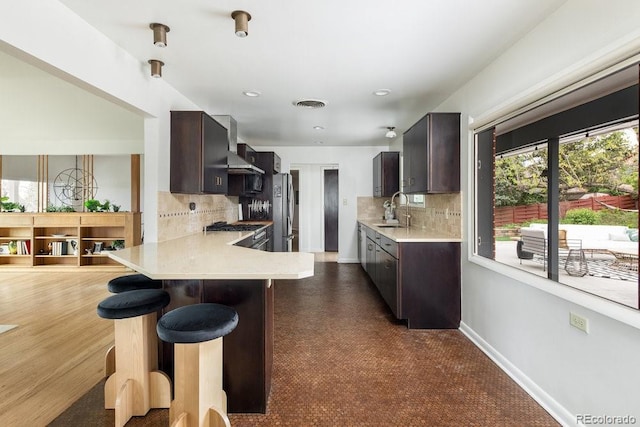 kitchen with a sink, light countertops, a kitchen breakfast bar, and dark brown cabinets