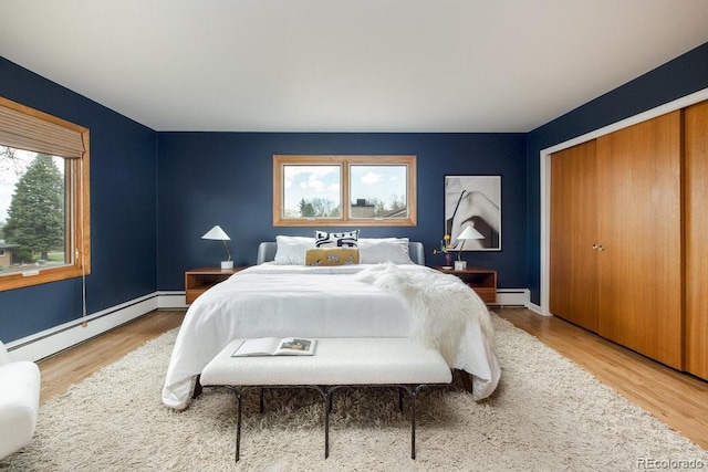 bedroom featuring light wood-type flooring, baseboards, a baseboard radiator, a closet, and a baseboard heating unit