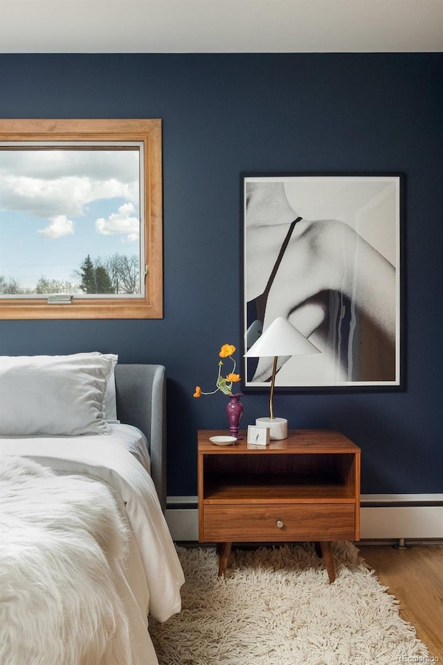 bedroom featuring baseboards, a baseboard heating unit, and wood finished floors