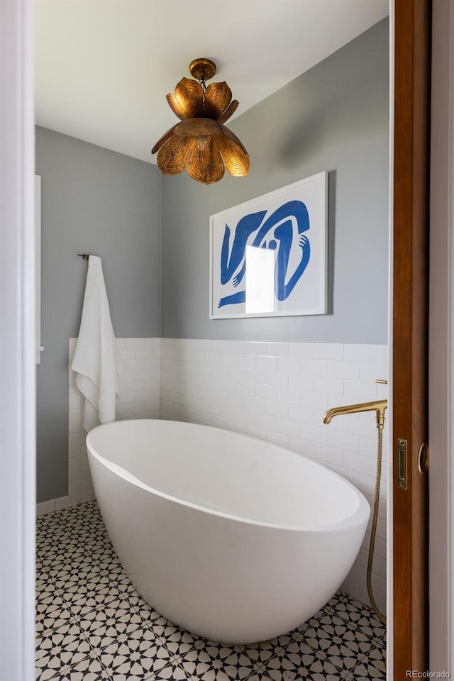 full bathroom with tile walls, a soaking tub, and a wainscoted wall