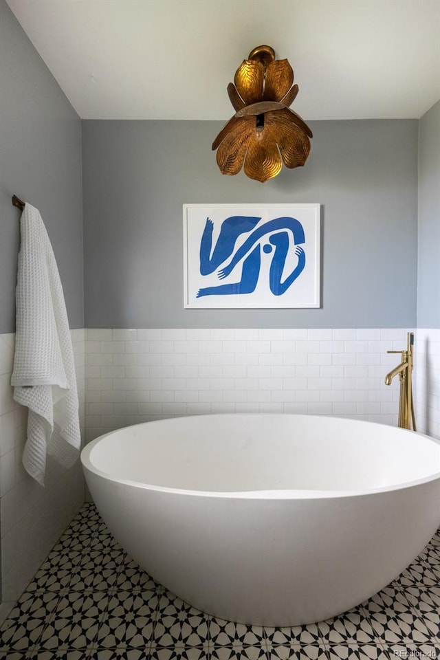 full bath with tile patterned floors, tile walls, wainscoting, and a soaking tub