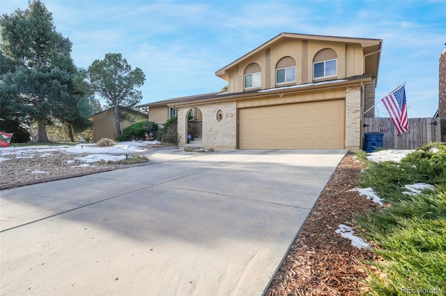 traditional-style home with driveway, a garage, brick siding, fence, and stucco siding