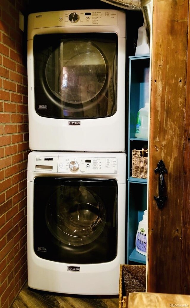 8211 Rocky Mountain Dr, Lakewood, CO 80214 - laundry room featuring brick wall, stacked washer / drying machine, and wood finished floors