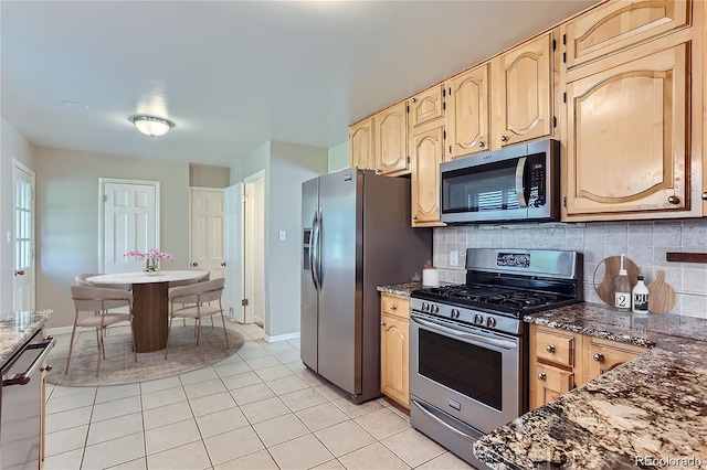 kitchen with stainless steel appliances, decorative backsplash, light tile patterned floors, dark stone counters, and light brown cabinetry