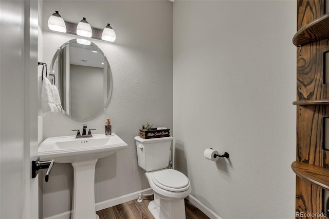 half bathroom featuring toilet, baseboards, a sink, and wood finished floors