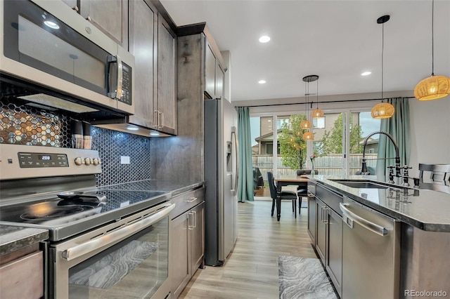 kitchen featuring decorative backsplash, pendant lighting, light wood-style floors, a sink, and appliances with stainless steel finishes