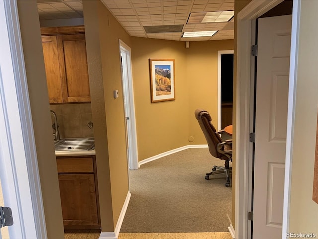 unfurnished office featuring carpet floors, a paneled ceiling, a sink, and baseboards