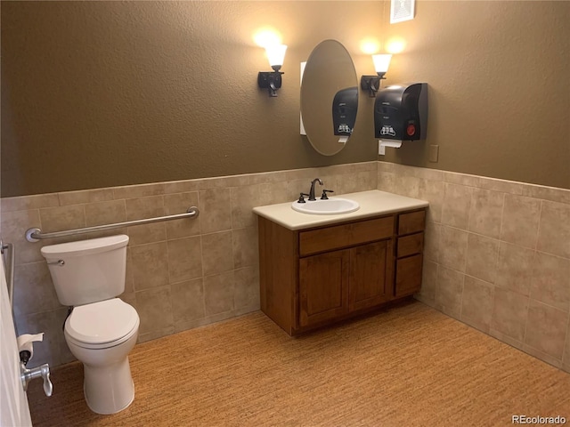 bathroom with visible vents, wainscoting, toilet, vanity, and tile walls