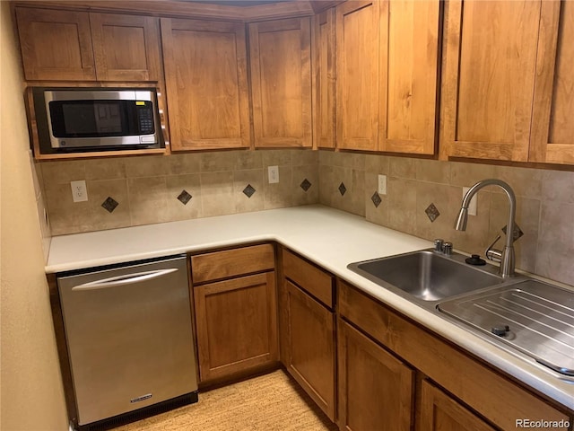 kitchen featuring decorative backsplash, appliances with stainless steel finishes, brown cabinets, light countertops, and a sink