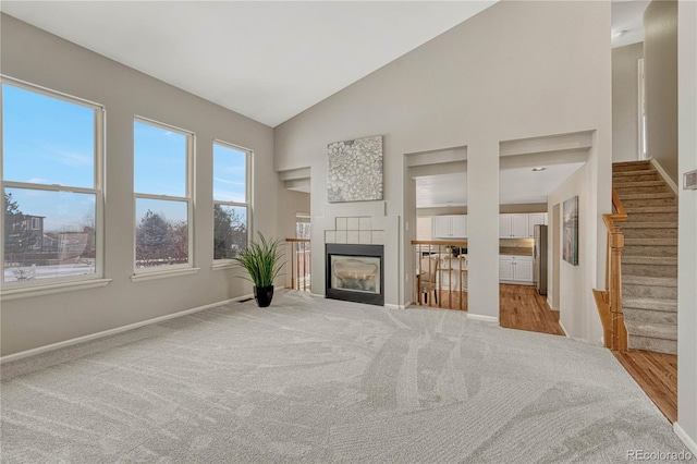 living room with high vaulted ceiling, light colored carpet, and a tile fireplace