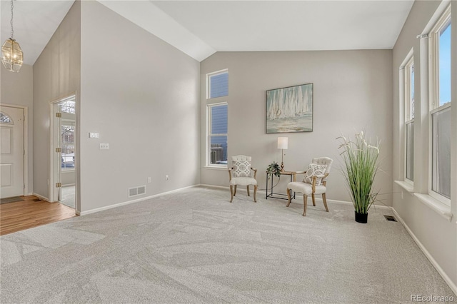 living area featuring an inviting chandelier, carpet floors, high vaulted ceiling, and a healthy amount of sunlight