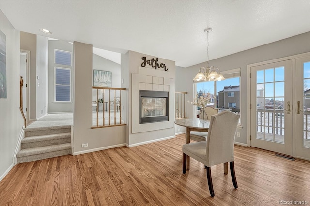 dining area featuring a tiled fireplace, light hardwood / wood-style flooring, and a chandelier