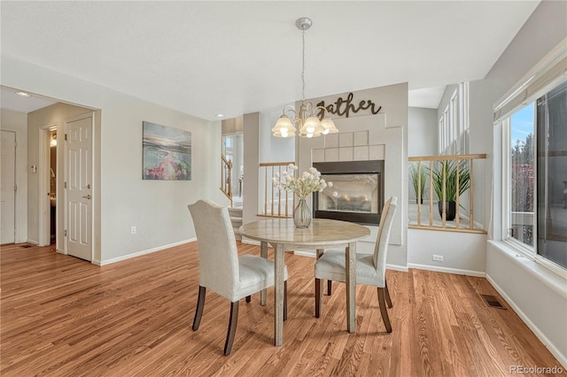 dining space with a fireplace, a chandelier, and light wood-type flooring