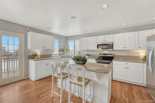 kitchen with appliances with stainless steel finishes, light wood-type flooring, a kitchen island, and white cabinets