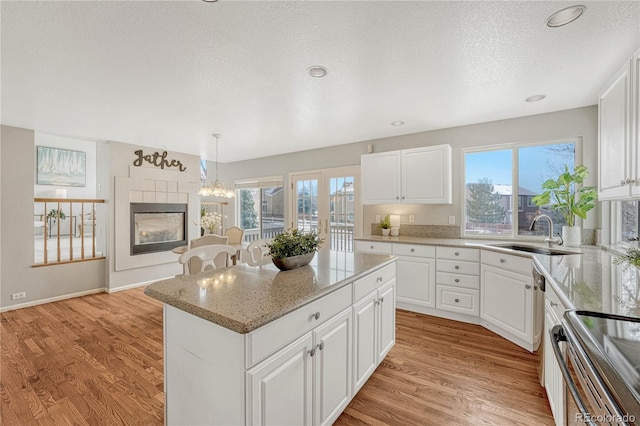 kitchen with a kitchen island, white cabinetry, sink, hanging light fixtures, and light wood-type flooring