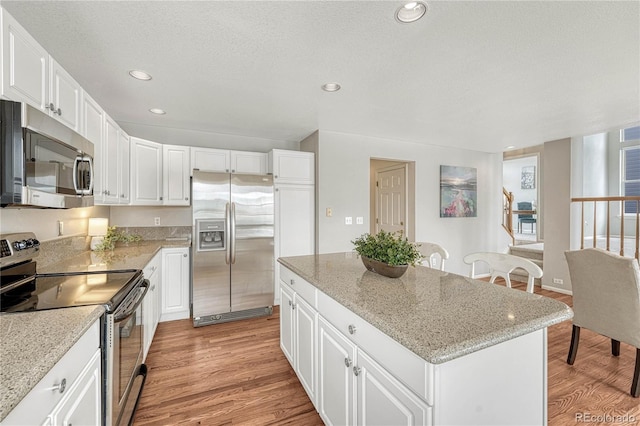 kitchen featuring stainless steel appliances, white cabinetry, a kitchen island, and light stone counters