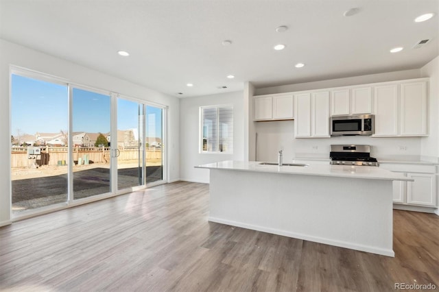 kitchen with sink, light hardwood / wood-style floors, stainless steel appliances, white cabinets, and a kitchen island with sink