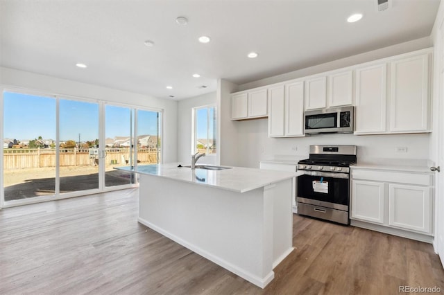 kitchen featuring white cabinets, a kitchen island with sink, stainless steel appliances, and light wood-type flooring