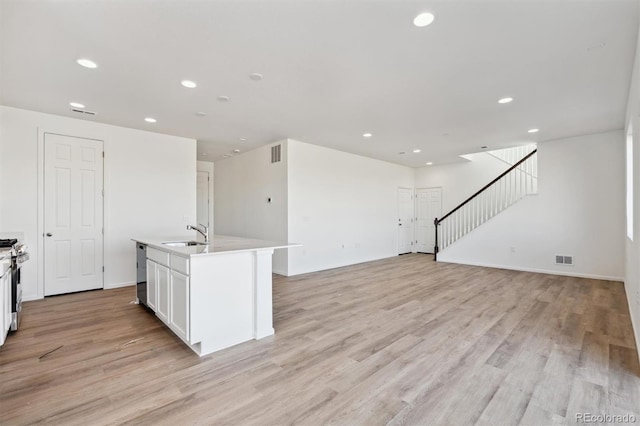 kitchen featuring a kitchen island with sink, stainless steel appliances, sink, white cabinets, and light hardwood / wood-style floors