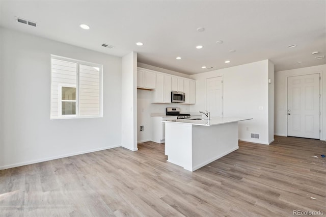 kitchen featuring appliances with stainless steel finishes, light wood-type flooring, a center island with sink, and white cabinets