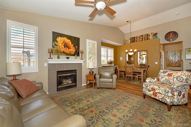 living room with hardwood / wood-style flooring, a fireplace, vaulted ceiling, and ceiling fan with notable chandelier